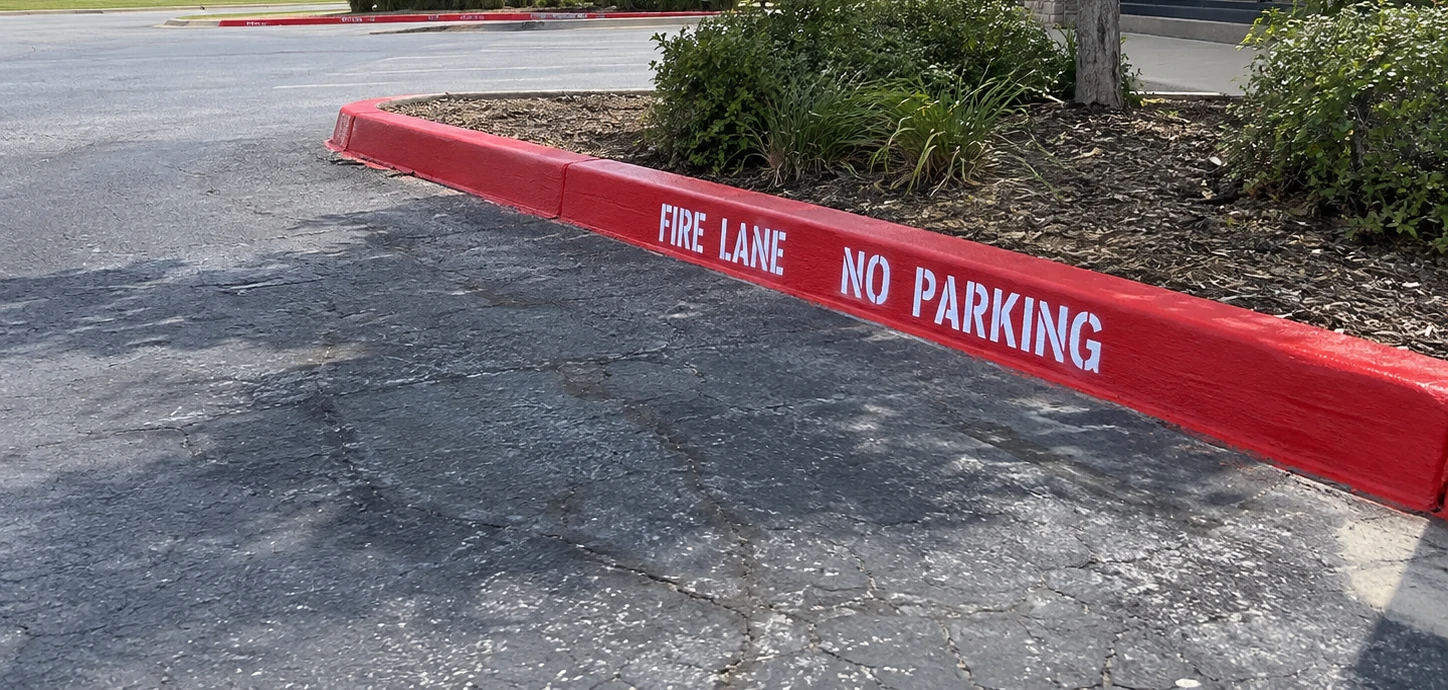 Red curb painted and stenciled with FIRE LANE NO PARKING in white letters